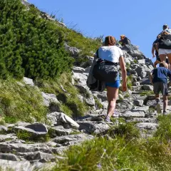 Rodzina wspina się kamienistym szlakiem. Dziecko idzie z przodu, a za nim dorośli. To ich wejście na Giewont.