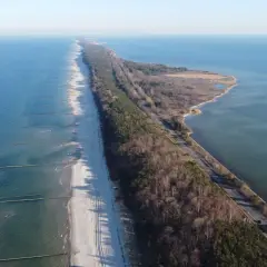 Wąski pas lądu, czyli **półwysep helski**, otoczony przez morze i zatokę. Na plaży widać falochrony, a w głębi las i drogę.