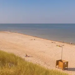 Słoneczna plaża w Kuźnicy nad morzem. Kilka osób odpoczywa na piasku, w oddali widać spokojne morze i błękitne niebo.