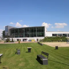 Nowoczesny budynek z przeszkloną fasadą, otoczony zielonym trawnikiem i ławkami. Idealne miejsce na rodzinne wycieczki i atrakcje dla dzieci w Kaliszu.
