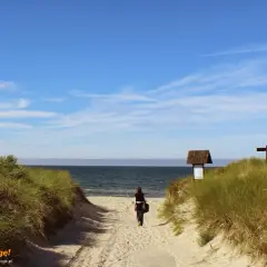 Kobieta idzie piaszczystą ścieżką na plażę. To idealne miejsce na chwilę wytchnienia podczas podróży samochodem.