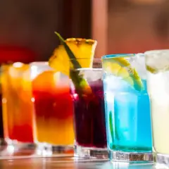 Rząd kolorowych, klasycznych drinków z lodem i owocowymi dekoracjami, gotowych do podania.