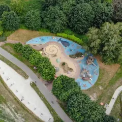 Kolorowy plac zabaw w kształcie fali z wielorybem i statkami pirackimi, otoczony zielenią. Idealne miejsce na zabawę dla dzieci w Łodzi.