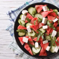 Orzeźwiająca sałatka z arbuzem i mozzarellą, z dodatkiem ogórka i rukoli, podana na czarnym talerzu.