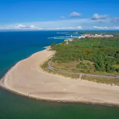 Widok na piaszczystą plażę i las, w oddali widać miasteczko i port. Widać też charakterystyczną latarnię morską Hel.