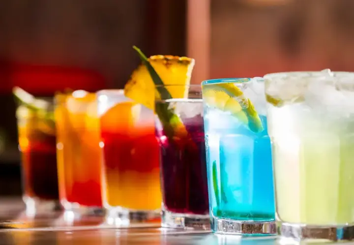 Rząd kolorowych, klasycznych drinków z lodem i owocowymi dekoracjami, gotowych do podania.