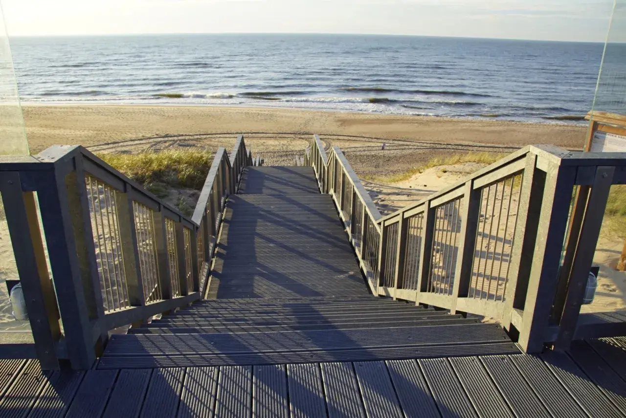 Schody prowadzące na plażę w Darłówku. Promenada z widokiem na morze i piasek.