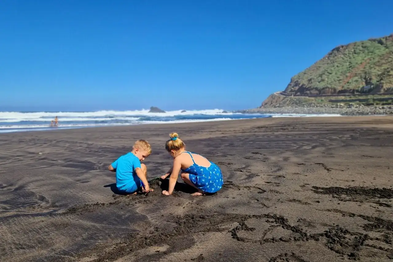 Dzieci budują zamki z piasku na czarnej plaży. Wspaniałe wspomnienia z Teneryfy z dziećmi.