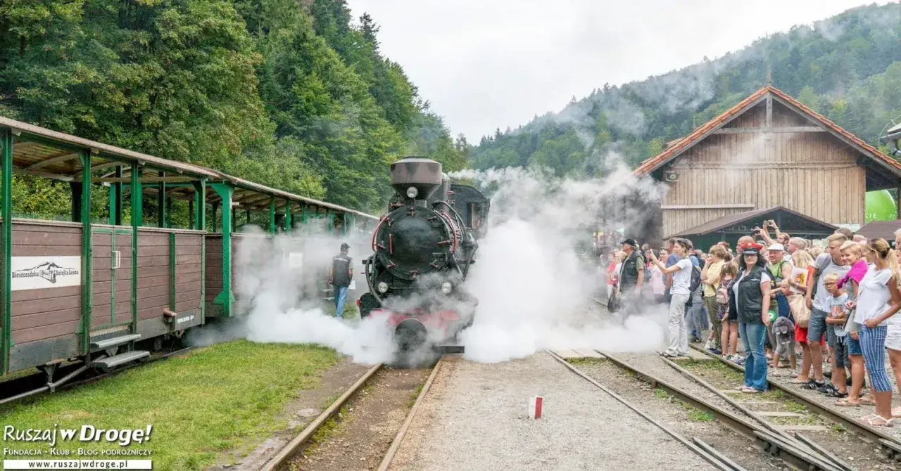 Para rodzinna wycieczka w Bieszczady z dziećmi. Parowóz z wagonami na tle leśnych wzgórz, tłum ludzi czeka na podróż.