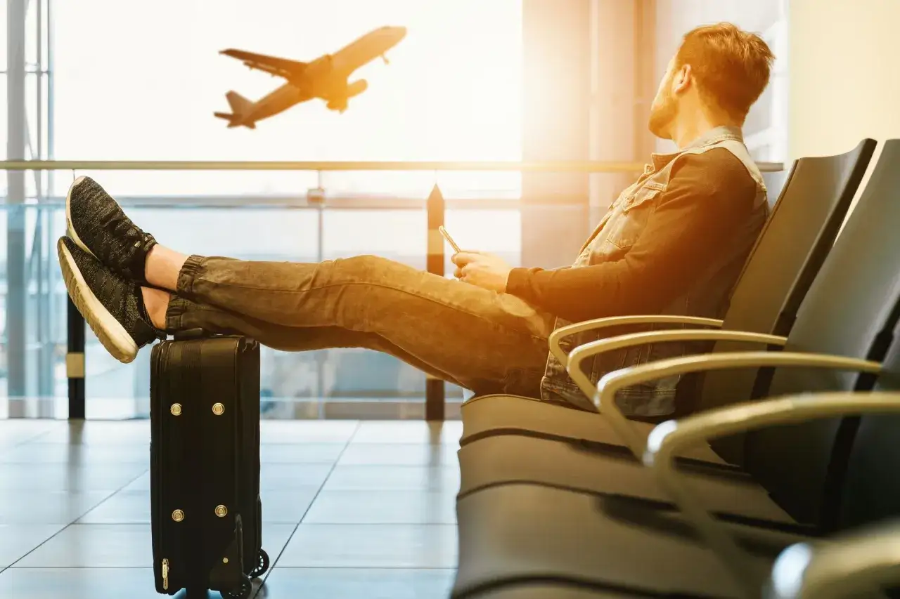 Mężczyzna z nogami na walizce czeka na lotnisku. Samolot startuje. Czyżby czekał na lot, który jest już w powietrzu? Overbooking?
